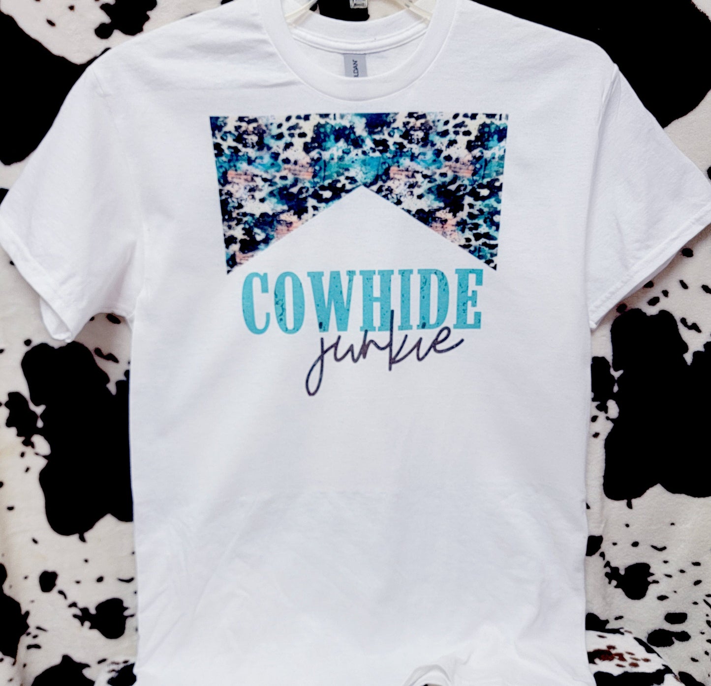 White t-shirt with 'Cowhide Junkie' text on a cow print background
