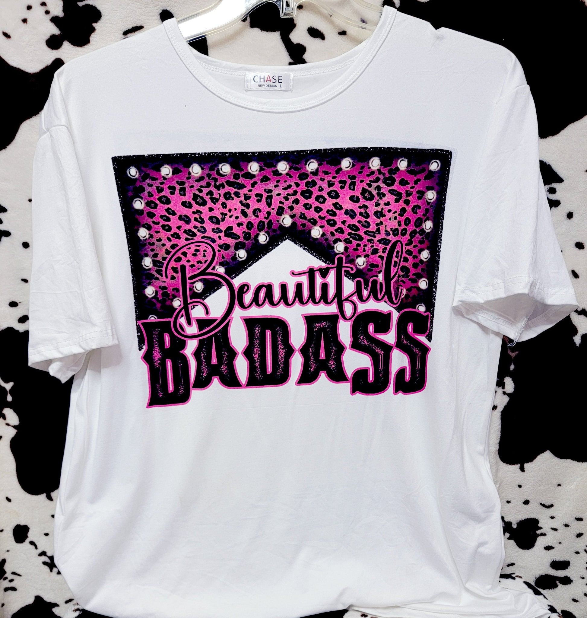 White t-shirt with pink and black graphic design on a cow print background