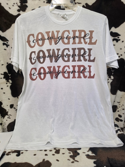A white short-sleeve t-shirt with 'COWGIRL' printed three times in a dusty rose-brown color, styled on a black and white cowhide background.